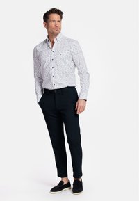 Chemise blanche à boutons avec un petit motif multicolore, associée à un pantalon noir slim et des chaussures noires à enfiler.