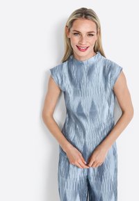 Tutina blu chiaro con collo alto e maniche a cappuccio. Presenta una texture a pieghe verticali e una silhouette aderente. Tessuto liscio e lucido.