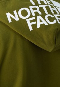 Groene hoodie van een gestructureerde stof. Heeft een voorste kangoeroezak en grote witte logo-tekst op de capuchon.