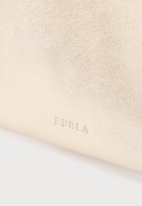 Bēša ādas soma ar teksturētu virsmu un nospiestu "FURLA" logotipu uz vienas puses. Vienkāršs dizains ar minimāliem metāla elementiem.