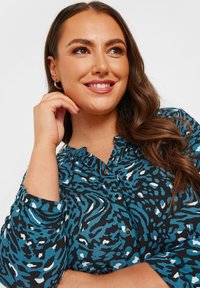 Blusa a maniche lunghe con un motivo animalier blu, nero e bianco, dotata di chiusura frontale con bottoni e leggero dettaglio del colletto.