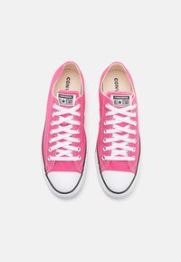 Pink canvas sneakers with white laces and rubber toe cap. Features "Converse All Star" logo on tongue and black outsole trim.