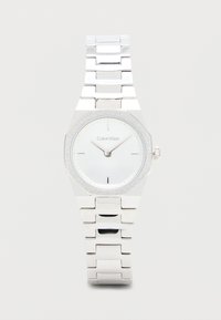 Montre-bracelet en argent avec un boîtier octagonal, un cadran blanc, des marqueurs d'heure minimalistes et une lunette scintillante ; présente une finition en métal poli.