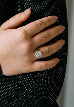Sterling-Silberring mit einem großen runden Diamanten in der Mitte, umgeben von kleineren Diamanten, getragen an einer Hand mit hellpinken Nägeln.