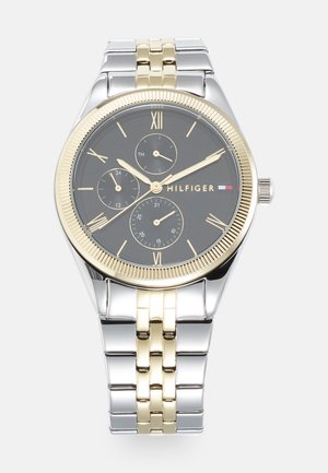 Montre-bracelet argentée et dorée avec un cadran noir, des chiffres romains, trois sous-cadrans et un bracelet en métal bicolore. Accent de lunette striée dorée.