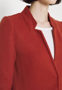 Rode wollen jas met een textuur afwerking, voorzien van een scherpe, ingesneden kraag en een schoon, open voorkant ontwerp. Strakke silhouet met naadloze schouders.