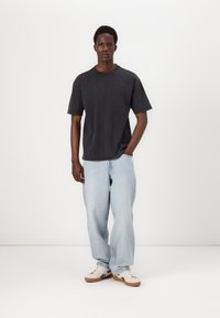 Tricou din bumbac negru cu mâneci scurte și guler rotund, asortat cu blugi din denim deschis, lejeri, și adidași casual.