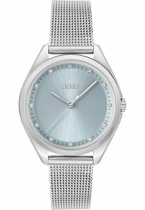 Montre à bracelet en maille argentée avec un cadran bleu clair, présentant une finition brossée et des index horaires en cristal, ainsi qu'un boîtier en argent poli.