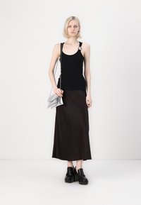 Melna bez piedurknēm tank top krekls ar sudraba gredzena detalizāciju, apvienots ar brūnu satīna maksi svārku un masīvām melnām platformas kurpēm. Sudraba plecu soma.
