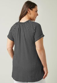 Schwarze Bluse mit Polka-Dots, die kurze Ärmel, einen gerafften Ausschnitt und einen lockeren Schnitt bietet. Sie hat eine glatte Stofftextur und einen längeren Rücken.