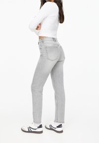 Jean gris taille haute avec une coupe droite, doté de poches arrière et d'un léger effet délavé. Associé à des baskets blanches.