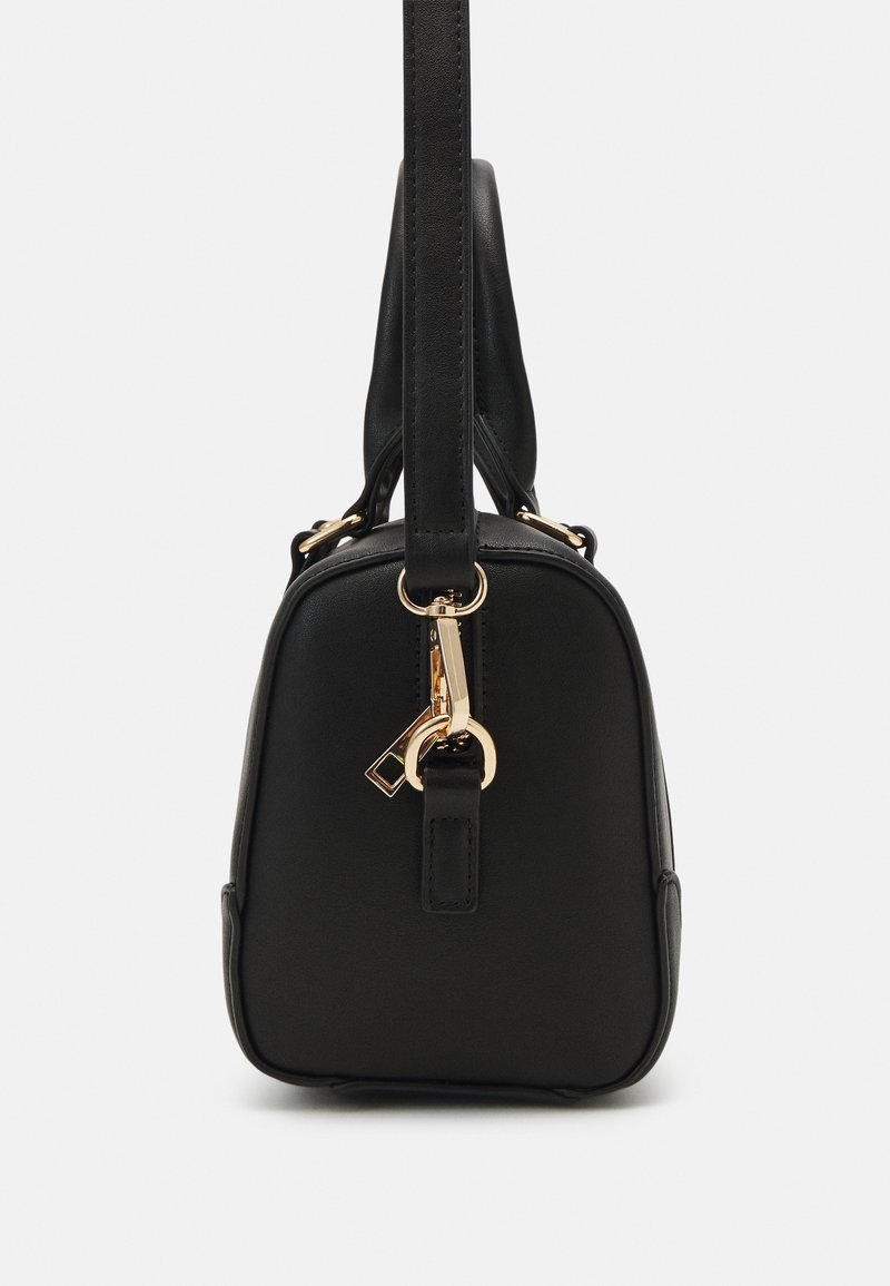 Sac à main en cuir noir avec forme structurée, fermeture à clip doré et détail anneau, vu de côté avec la poignée s'étendant vers le haut.