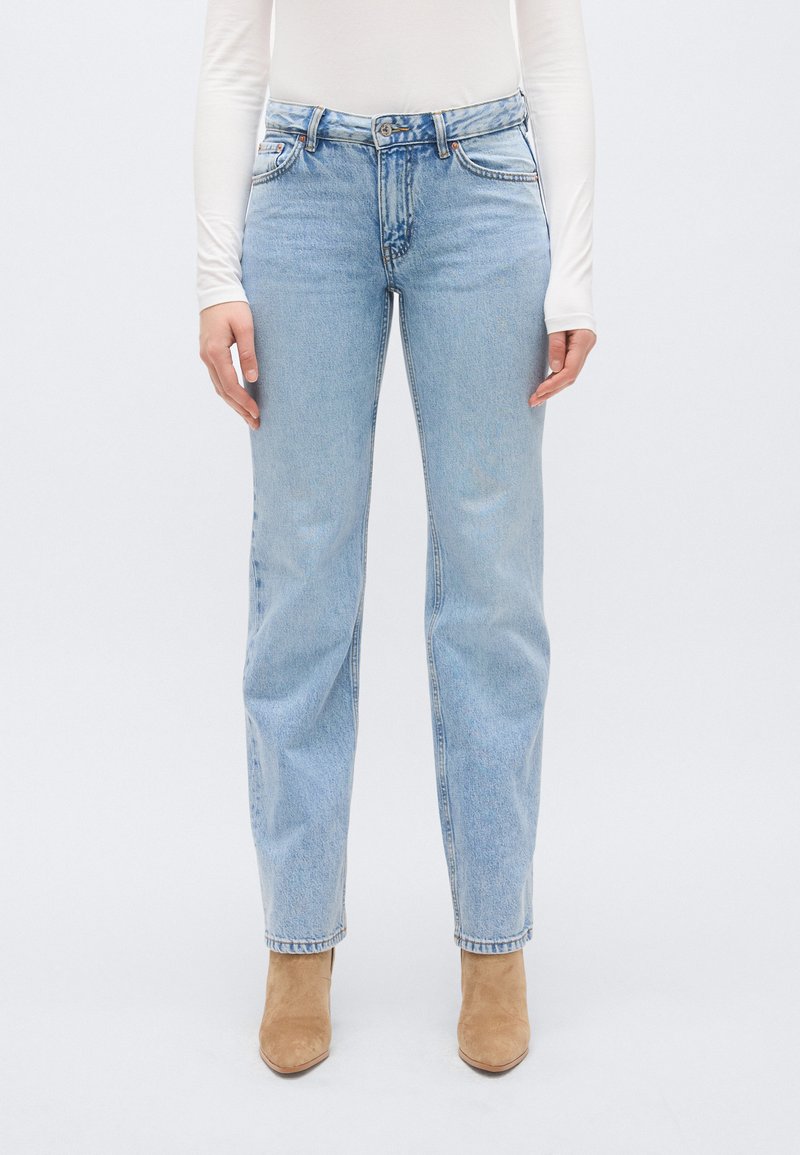 Blugi din denim albastru deschis cu design cu picior drept, cinci buzunare și închidere cu nasture. Tivul este ușor ciufulit, cu un finisaj estompat.