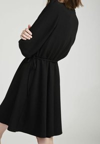 Svart klänning med långa ärmar, midjebälte och utsvängd kjol. Slätt tyg med enkel struktur. Minimalistisk design, passar för olika tillfällen.