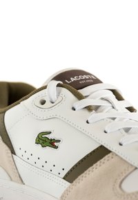 Sneaker bianca in pelle con accenti verdi, pannello in suede beige e logo coccodrillo ricamato. Presenta lacci bianchi e dettagli perforati.