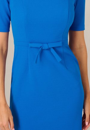Blaues figurbetontes Kleid mit kurzen Ärmeln und einem schmalen Gürtel, der in einer Schleife an der Taille gebunden ist, dargestellt von der Mitte des Oberkörpers bis zu den Hüften.