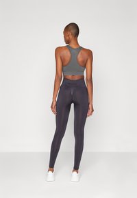 Grå sportsbh med racerback-design, kombinert med høyhåndte, mørke tights med en glatt tekstur og subtil merkevare ved midjen.