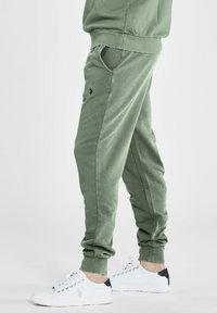 Gröna bomullsjoggers med sidofickor, tapered fit och broderad logotyp. Matcher med vita sneakers med svarta accenter.