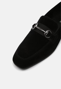 Mocassins en suede noir avec un orteil carré, dotées d'une bande en satin noir mat et d'accents en métal argenté pour un design raffiné.