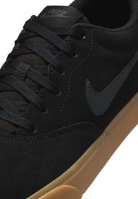 Zapatillas de ante negro con acentos de tejido texturizado, con el logo de Nike en gris oscuro y una suela de goma. Diseño con cordones.