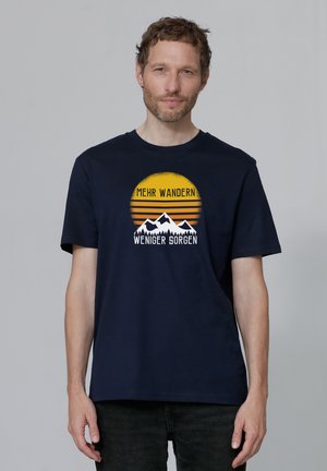 Navyblauwe katoenen t-shirt met een grafisch ontwerp van bergen en een zon, met de tekst "MEHR WANDERN" en "WENIGER SORGEN."