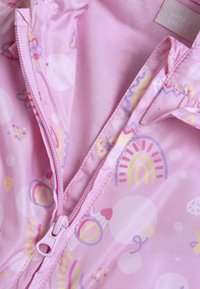 Imperméable rose avec une fermeture éclair. Présente des motifs multicolores comprenant des cercles, des cœurs et des arc-en-ciel sur un tissu lisse et brillant.