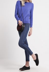 Jasnofioletowy sweter z dzianiny, dopasowany, z okrągłym dekoltem; ciemnoniebieskie skinny jeansy; czarna okrągła torebka na ramię; czarne płócienne buty na sznurówki.