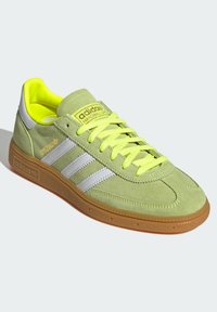 Gröna mockasneakers med vita ränder, klara gula accenter och en sula av gummirubber. Har vadderad krage och texturerat snörningsområde.