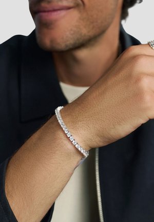 Silver bracelet with a row of clear, round gemstones along a flexible band, worn on a wrist with a light skin tone.