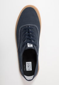 Sneaker in tela blu con cuciture bianche e design con lacci. Presenta una suola in gomma marrone e un'etichetta con logo bianco sulla linguetta.