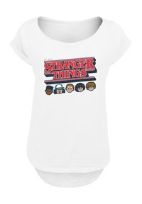 White t-shirt featuring a large "Stranger Things" graphic in red and blue, with five cartoon character faces below the text. Soft fabric, loose fit.