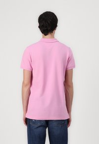 Rosa pikétröja med klassisk krage, korta ärmar och en V-formad sömdetalj på baksidan, i kombination med blå jeans.