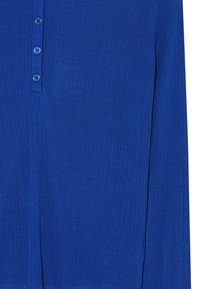 Modrá pletená blúzka s dlhým rukávom, ktorá má zapínanie na štyri gombíky. Tkanina má rebrovanú textúru. Žiadne viditeľné vzory alebo akcenty.