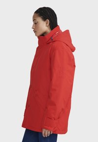Rote isolierte Jacke mit Kapuze, Druckknopfverschlüssen und dezenten Logo-Details am Ärmel. Verfügt über seitliche Taschen und eine lässige Passform.
