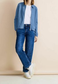 Jasnoniebieska rozpinana polarowa kurtka na białej koszulce, w połączeniu z niebieskimi jeansami o prostym kroju i białymi trampkami. Gładkie tekstury materiałów.