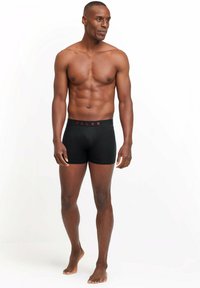 Boxer-briefs noirs avec une ceinture rouge arborant le logo "FALKE", fabriqués dans un tissu lisse et extensible, conçus pour le confort et l'ajustement.