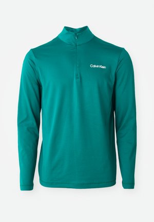 Top de manga larga en color azul verdoso con cuello alto y media cremallera, que presenta una tela texturizada y un logo blanco en el lado izquierdo del pecho.