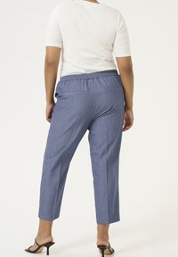 Siniset, kevyet housut, joissa on joustava vyötärö, suorat lahkeet ja takataskut. Materiaalissa on hieno rakenne, yhdistettynä mustiin sandaaleihin.