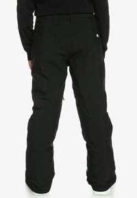 Čierne snehové nohavice s hladkou textúrou, širokým strihom, nastaviteľným pásom a logom na zadnej strane. Disponujú spevnenými manžetami.