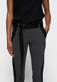 Grijze joggingsbroek met een zwarte zijpaneel, voorzien van een zwarte verstelbare riem, slim fit en voorzakken. Zachte stof met een gladde textuur.