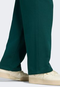 Groene joggingbroek met een recht model, gemaakt van zachte stof, gecombineerd met crèmekleurige sneakers met textuurelementen.