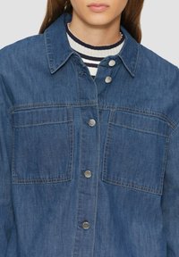 Dunkelblaue Jeansjacke mit Knopfleiste, zwei Brusttaschen und kragenförmigem Ausschnitt. Verfügt über silberne Druckknöpfe und sichtbare Nähte.
