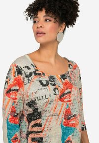 Haut multicolore à coupe décontractée, avec un imprimé graphique de lèvres et de texte, col rond et manches trois-quarts. Tissu texturé.