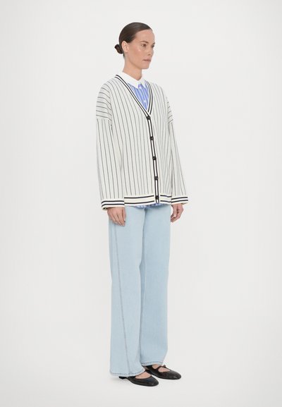 Cardigan rayé en crème et bleu marine, avec un col en V, des manches surdimensionnées et une fermeture à boutons, associé à un jean large bleu clair et des ballerines.
