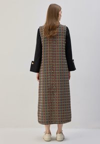 Ilga juoda su raštais su daugiabriauniais spalvotais geometriniais raštais. Turi laisvą kirpimą, pilną ilgį ir auksinius mygtukų akcentus ant rankovių.