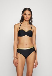 Juodas bikinis su bandeau stiliaus viršumi, papuoštu auksine apdaila ir centrine detale. Apatinė dalis turi atitinkamą auksinę juosmens juostą ir šonines raišteles.