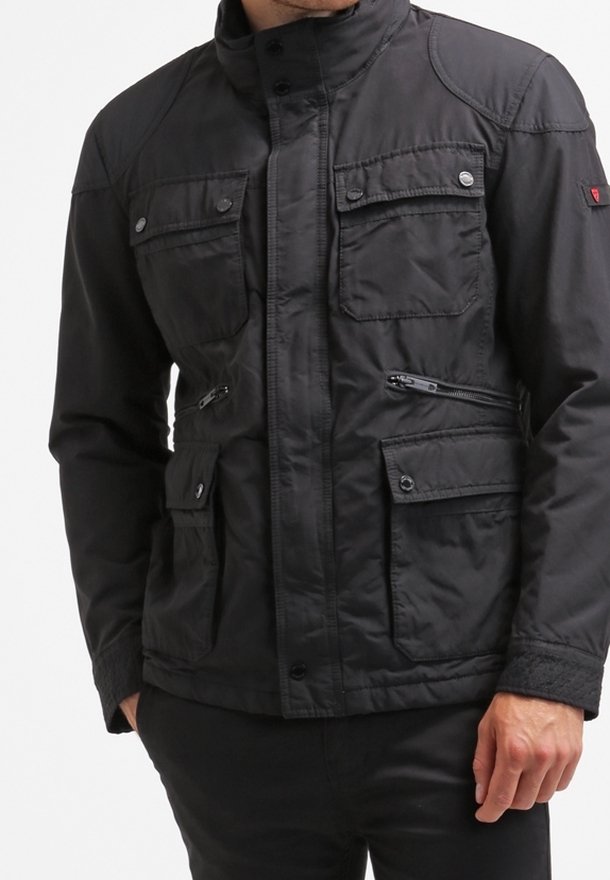 Svart jacka med hög krage, flera framfickor och dragkedjedetaljer. Tillverkad av ett texturerat tyg med en något glänsande yta.