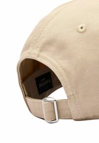 Beige bomullsbasketmössa med en rundad skärm, texturerad tyg och ett silverfärgat justerbart spänne på baksidan.