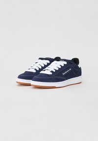 Navy blue sneakers made of suede with white laces, rubber sole, and a tan outsole. Features a stitched design and a logo on the side.