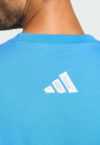 Hellblaue Baumwoll-T-Shirt mit Rundhalsausschnitt. Mit einem weißen Adidas-Logo auf dem oberen Rücken bedruckt. Glatte Textur.